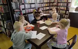 Dzieci przy stołach wykonują karty pracy i kolorują kredkami na kartkach świnki.