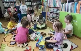 Dzieci siedzą ze swoją Panią na dywanie i bawią się pluszowymi książeczkami.