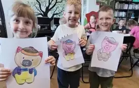 Dziewczynka i dw&oacute;ch chłopc&oacute;w pokazują na kartkach swoje pokolorowane świnki.