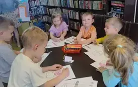 Dzieci przy stole kolorują kredkami na kartkach świnki.