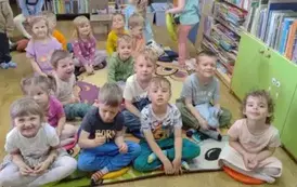 Dzieci siedzą na siedziskach i słuchają bajki czytanej przez bibliotekarkę.