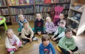 Dzieci siedzą na siedziskach w bibliotece i słuchają bajki.