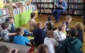 Dzieci siedzą przy stoliku i na dywanie i słuchają bajki, ktorą czyta im gościnnie kierowca przewoz&oacute;w szkolnych Pan Wojciech Formela