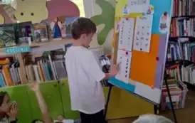 Dzieci siedzą na dywanie,a z przodu przy tablicy stoi chłopiec i uzupełnia kartę pracy. Obok siedzi Pani sołtys i patrzy na chłopca.