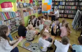 Dzieci siedzą na dywanie i słuchają bajki, kt&oacute;rą im czyta Pani sołtys wsi Tomaszewo. Na wprost stoi metalowa tablica przystrojona w kolorowe kartki  z napisem &quot; Cała Polska Czyta Dzieciom&quot;.