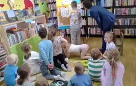 Dzieci siedzą na siedziskach, z przodu przy tablicy stoi chłopiec i uzupełnia na niej przyczepioną kartę pracy. Sołtys stoi przy nim pochylony.