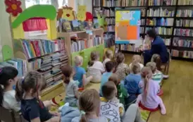 Dzieci siedzą na dywanie i słuchają bajki, kt&oacute;rą im czyta sołtys wsi Pinczyn. Na wprost stoi metalowa tablica przystrojona w kolorowe kartki  z napisem &quot; Cała Polska Czyta Dzieciom&quot;.