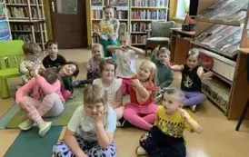 Dzieci siedzą na podłodze, za nimi siedzi gościnnie Pani Małgorzata, kt&oacute;ra czytała bajkę i trzyma książkę pt. "Sprzątanie świata - dbam o środowisko"