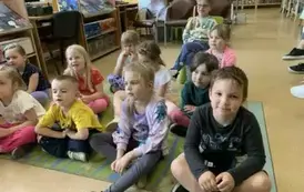 Dzieci siedzą na dywanie i słuchają bajki, kt&oacute;rą gościnnie czyta Pani Małgorzata Milewska