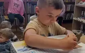 Chłopiec stoi przy biurku i wkłada ruchomą część do książki. Reszta dzieci siedzi.