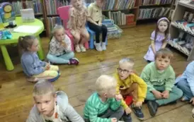 Dzieci siedzą na siedziskach i krzesełkach i słuchają bajki.
