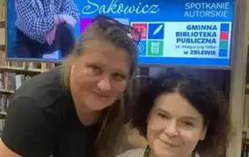 Czytelniczka jest pochylona twarzą blisko siedzącej Anny Sakowicz. Nad nimi jest wyświetlony ekran z plakatem ze spotkania.