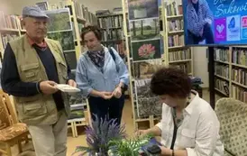 Przy stoliku pisarki stoi kobieta z mężczyzną, kt&oacute;ry trzyma książkę Anny Sakowicz do podpisu.