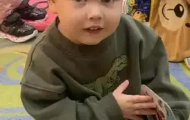 Chłopiec w blond włosach i w zielonej bluzie przegląda tekturową książeczkę. 