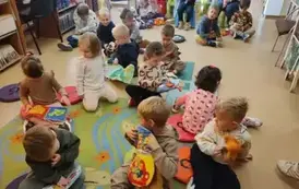 Dzieci siedzą na dywanie i siedziskach bawiąc się pluszowymi książeczkami.