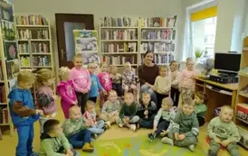 Dzieci siedzą w p&oacute;łkolu razem z bibliotekarką.