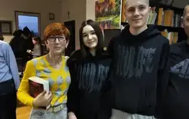 Pani w rudych włosach stoi z dziewczyną i chłopakiem w czarnych bluzach. Pani w rudych włosach trzyma nową książkę pisarza. Uśmiechają się.