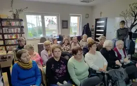 Twarze senior&oacute;w siedzących na krzesłach, z boku stoi bibliotekarka.