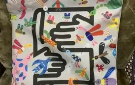 Biały materiałowy worek ze ściągaczem u g&oacute;ry, w kolorowe zwierzątka, a po środku dwie czarne rączki obejmujące książkę.