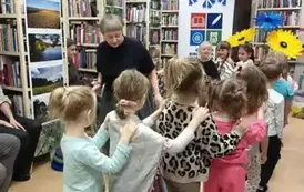 Dzieci idą wężykiem jeden za drugim za Panią Małgosią trzymając się za ramiona.