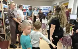 Dzieci stoją w k&oacute;łeczku wraz ze swoimi rodzicami i z Panią z biblioteki.