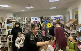 Dzieci idą ze swoimi rodzicami jeden za drugim w koło biblioteki.