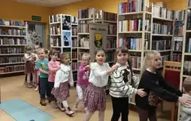 Dzieci idą w koło biblioteki jeden za drugim trzymając się za ramię.