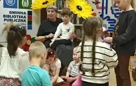 Dzieci siedzą na dywaniku i bawią się jakimiś przedmiotami ,a na kolanach Pani Małgosi siedzi chłopiec w ciemnych włosach.