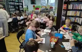 Trzy stoły pełne dzieci, kt&oacute;re uzupełniają miosiwe sudoku. Z lewej strony widać Panią, kt&oacute;ra pomaga przy stole. 