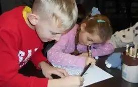 Chłopiec w blond włosach i w czerwonej bluzie z koleżanką uzupełniają przy stole misiową kartę pracy.