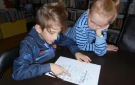 Chłopiec z dziewczynką przy stole patrzą na misiową kartę pracy. Chłopiec pokazuje coś palcem na kartce.