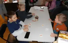 Dzieci przy białym stole układają karty z misiami.