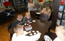 Dzieci przy stołach układają karty z misiami, obok stoi ich Pani.