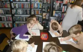 Dzieci siedzą przy stole i uzupełniają misiowe karty pracy. Przy stole stoi ich Pani.