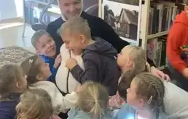 Na dywanie siedzi kobieta przebrana za misia Pandę, a przy niej dzieci, kt&oacute;re się do niej przytulają.