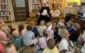 Dzieci siedzą na dywanie i patrzą do przodu, gdzie siedzi Pani przebrana za misia Pandę. Obok na fotelu i podłodze są misie, a z przodu tablica korkowa z grafikami misiowymi.