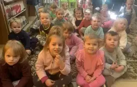 Dzieci siedzą na dywanie i się uśmiechają.