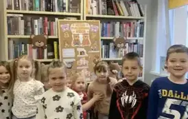 Dzieci stoją przy korkowej tablicy przystrojonej misiowymi grafikami. U g&oacute;ry na szafie są kolorowe balony.