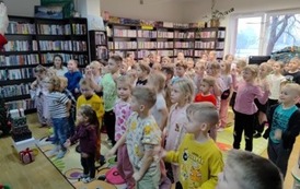 Spora grupa dzieci stoi na dywanie i naśladują ruchy taneczne elf&oacute;w.