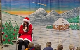 Po środku na krześle siedzi zasmucona pomocnica świętego Mikołaja. W tle g&oacute;rski zaśnieżony pejzarz.