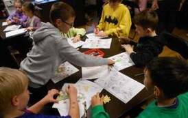 Dzieci siedzą przy stołach i uzupełniają świąteczne karty pracy