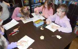 Dziewczynki siedzą przy stole i uzupełniają świąteczne karty pracy