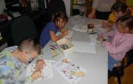 Dzieci przy białym stole uzupełniają świąteczne karty pracy