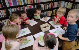 Dzieci przy stole kolorują kredkami na kartkach choinki.