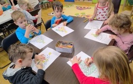 Dzieci przy stole kolorują kredkami na kartkach choinki.