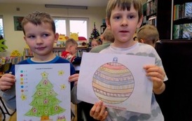 Dwoje chłopc&oacute;w stoi i pokazuje swoje pokolorowane prace : choinkę i bombkę.