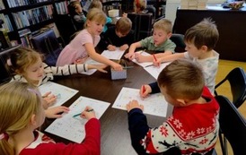 Dzieci siedzą przy dw&oacute;ch stołach i kolorują choinkę według podanego kodu