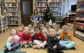 Dzieci siedzą przy choince z Bibliotekarką, ktora trzyma książeczkę pt "Magiczne Święta"