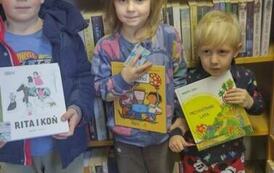 Dziewczynka stoi z dwoma swoimi braćmi po bokach. Trzymają swoje nowe książki jakie otrzymali w prezencie od biblioteki.
