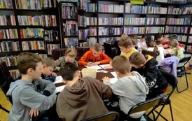 Dwa stoły pełne siedzących przy nich dzieci, kt&oacute;re rozwiązują krzyż&oacute;wkę wpisując hasła kredkami.